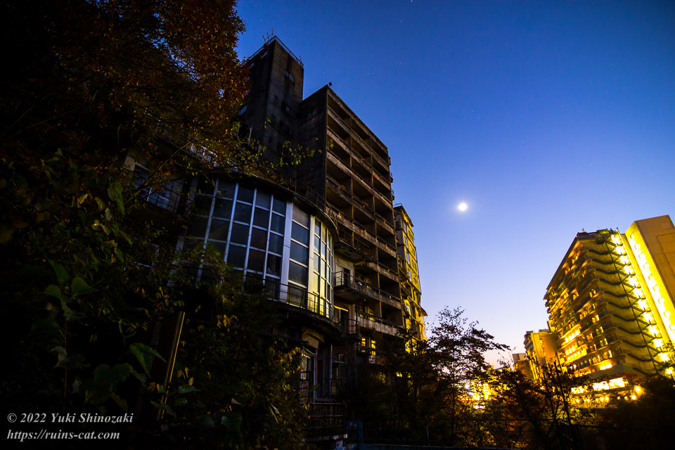 月下に照らされるきぬ川館本店の巨大廃墟と、煌々ときらめく対岸の現役ホテル